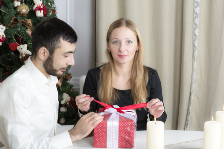 Portrait of a man and woman near the Christmas tree. The wife opens the gift from her husband.の写真素材