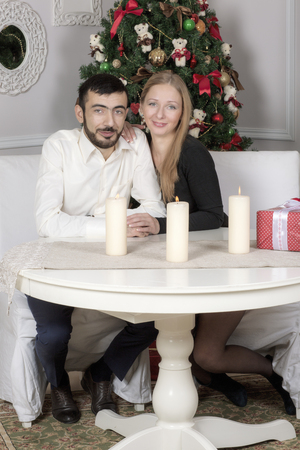 Portrait of a man and woman near the Christmas tree. Wife and husband sitting at the table.の写真素材