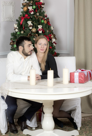 Portrait of a man and woman near the Christmas tree. Wife and husband sitting at the table.の写真素材