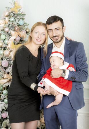 Family portrait near the Christmas tree. The child is dressed in the costume of Santa Claus.の写真素材