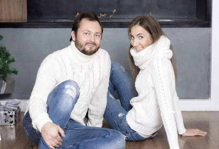 Portrait of husband and wife in white sweaters. Man and a woman sitting near the fireplace.の写真素材