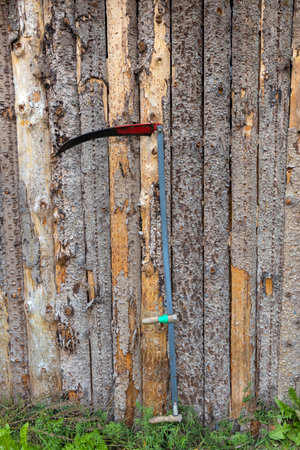 A scythe for mowing grass stands at a wooden fence. Village. Rustic style, Natural backgroundの写真素材