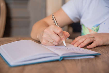 Close up view of woman sit at table hold pen take notes to paper notebook working studying