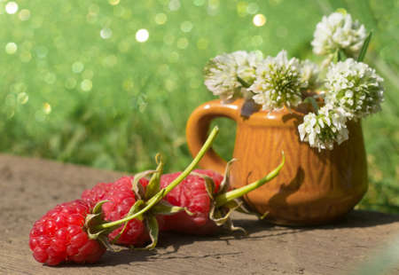 Red raspberries lie near a vase of flowersの写真素材