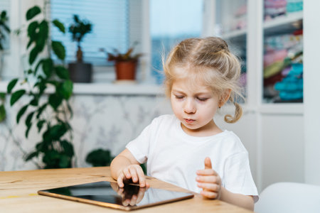 a little girl is sitting at a table with a tablet with her hands raised in the air smiling and happy, experiencing happinessの写真素材