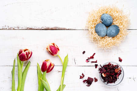 easter eggs, painted with natural dyes, hibiscus flowers, karkade tea, on a white aged wooden...