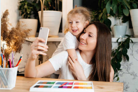 my daughter and mother are sitting at a table with colored plasticine for modeling and talking via video link. the concept of the holiday, mothers Day and childrens Dayの写真素材