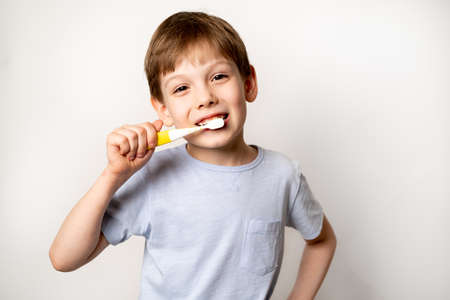 Little boy with a toothbrush on a white background brushes his teeth and smiles close-up, the...