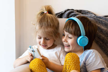 Brother and sister sit at home on the couch with smartphones, girl in headphones, concept kids and modern technology.の写真素材