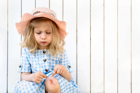 Little beautiful blonde girl, sad with broken knee on white wooden backgroundの写真素材
