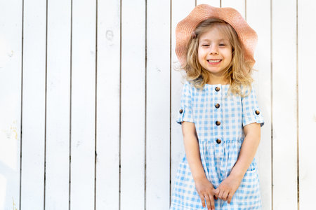 Happy little girl stands by the white wooden wall and smilesの写真素材