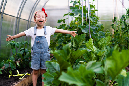 a little happy blonde girl in a greenhouse with her hands up rejoices, plant care, gardening concept for childrenの写真素材