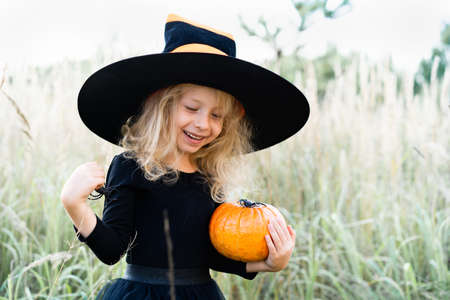 little blonde girl in a black suit and witch hat, Halloween with a pumpkin in her handsの写真素材