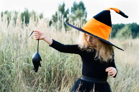 little blonde girl in a black suit and a witch hat with a black rat in her hands, Halloween, a fun holidayの写真素材