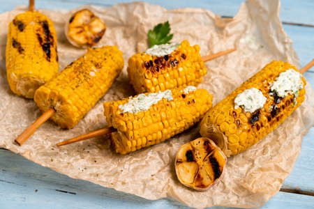 grilled corn on a blue wooden table with green sauceの写真素材