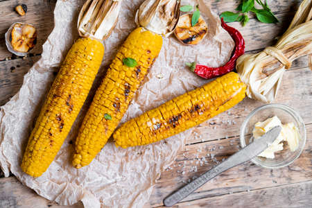 grilled corn with tied cobs on wooden boards with butter and spices