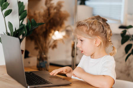 a small blonde girl with a laptop sits at a table and smiles