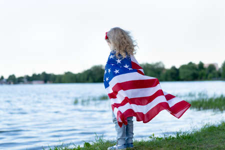 little girl with the American flag in nature, the concept of patriotism and the holiday of...