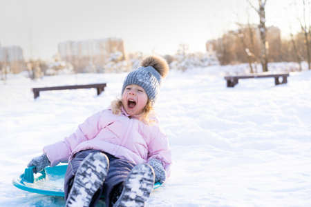little girl rides down the slide on the ice, cheerful child, emotions from winter funの写真素材