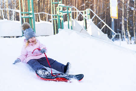 little cute girl learning to ride a childrens snowboard, winter sports for the child, safety of...