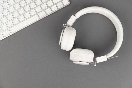 Background music or podcast with headphones and a computer keyboard on a gray table, flat. Top view,...