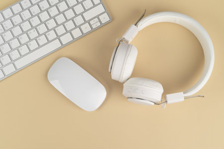 Background music or podcast with headphones and a computer keyboard on a beige table, flat. Top...