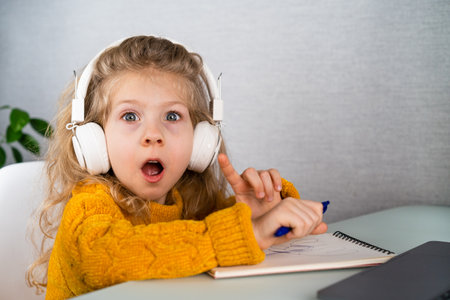a little blonde girl in headphones smiling and playing the synthesizer, the concept of teaching children musicの写真素材