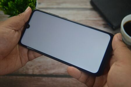 Close up Hands on blank screen smartphone on wooden tableの写真素材
