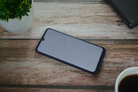 Blank screen smartphone between coffee cup an vase on wood tableの写真素材