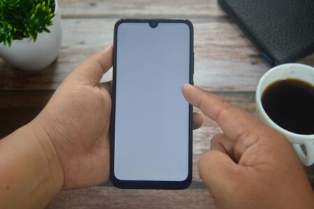 Close up Hands on blank screen smartphone on wooden tableの写真素材