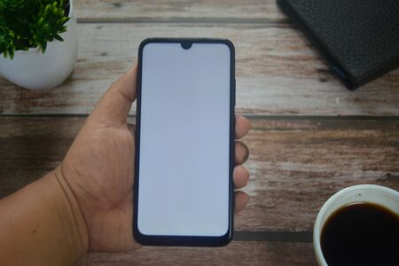 Close up Hands on blank screen smartphone on wooden tableの写真素材