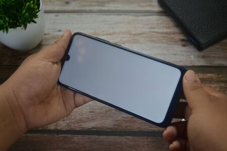 Close up Hands on blank screen smartphone on wooden tableの写真素材