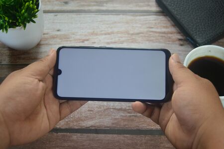 Close up Hands on blank screen smartphone on wooden tableの写真素材