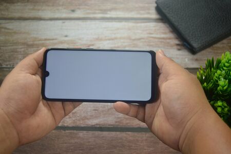 Close up Hands on blank screen smartphone on wooden tableの写真素材