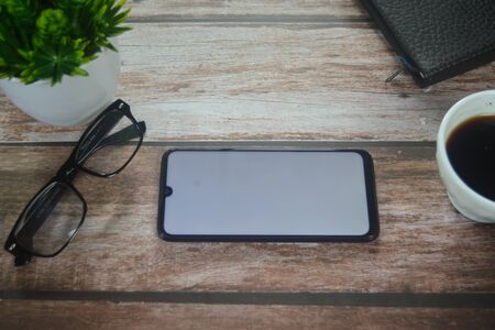 Blank screen smartphone between coffee cup an vase on wood tableの写真素材