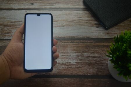 Close up Hands on blank screen smartphone on wooden tableの写真素材