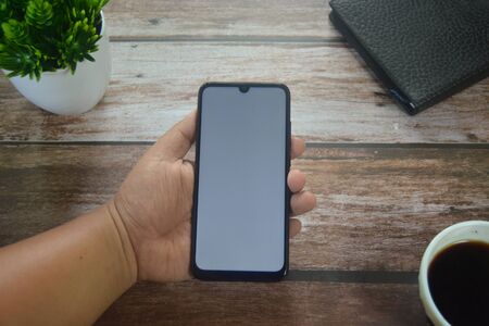 Close up Hands on blank screen smartphone on wooden tableの写真素材