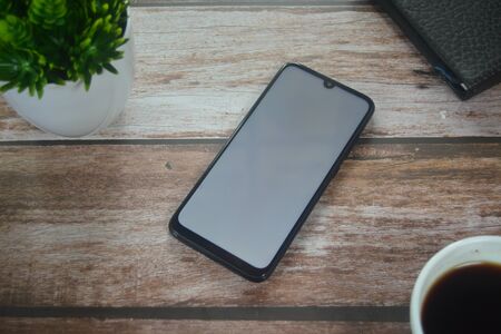 Blank screen smartphone between coffee cup an vase on wood tableの写真素材