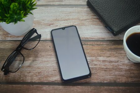 Blank screen smartphone between coffee cup an vase on wood tableの写真素材
