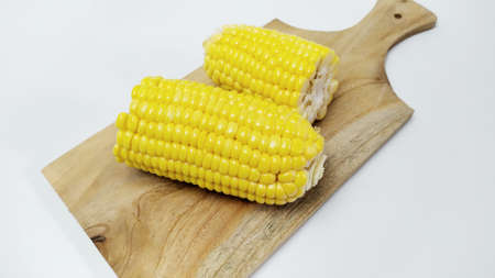 Close up fresh yellow sweet corn on cutting board isolated on white backgroundの写真素材