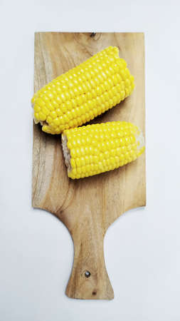 Close up fresh yellow sweet corn on cutting board isolated on white backgroundの写真素材