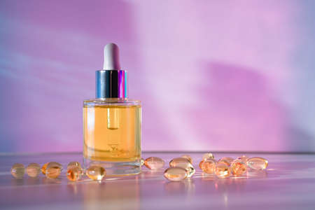 Yellow face oil in glass bottle with beauty capsules on light pink and blue background with geometric shadows. Front viewの写真素材