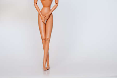 Nude doll covering pelvic area on white background. Female figure having UTI problems.