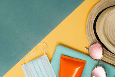 Beach composition with straw hat, mask, sunglasses, sunscreen. Paper sand ans sea. Holiday pandemic...
