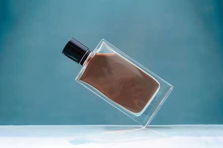 Suspended glass perfume bottle with black cap on blue background. Anti-gravity front viewの写真素材