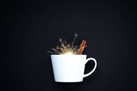 Blank white ceramic mug on black background with sparks and cinnamon stickの写真素材