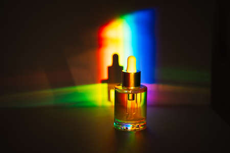 Yellow face oil with a dropper bottle in rainbow prism light. Side view
