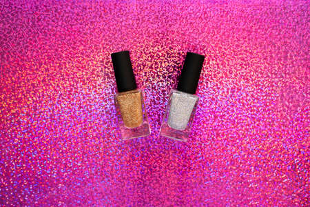 A pink sparkle background with gold and silver holographic nailpolish in glass bottle and black cap