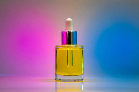 Yellow face oil in glass bottle on light pink and blue background with geometric shadows. Front viewの写真素材