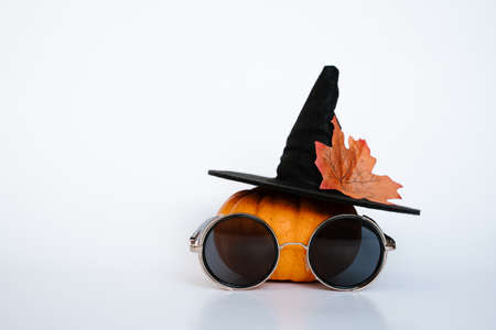 creative small orange pumpkin with black witch hat autumn leaf and black sunglasses on white isolated background. Halloween and Thanksgiving seasonの写真素材
